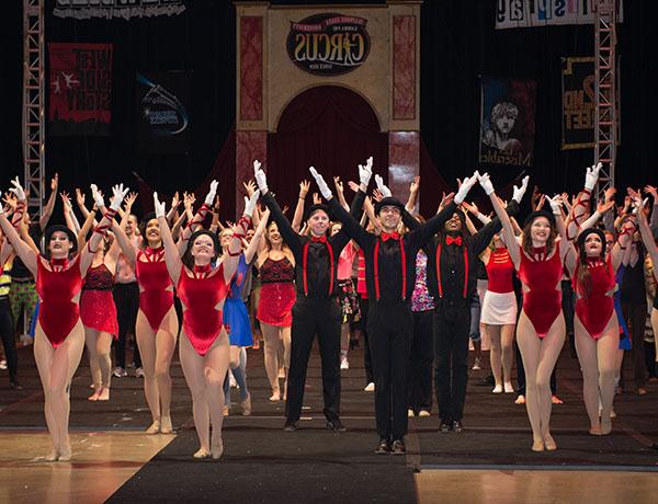 Circus performers pose in a group with their arms in the air.